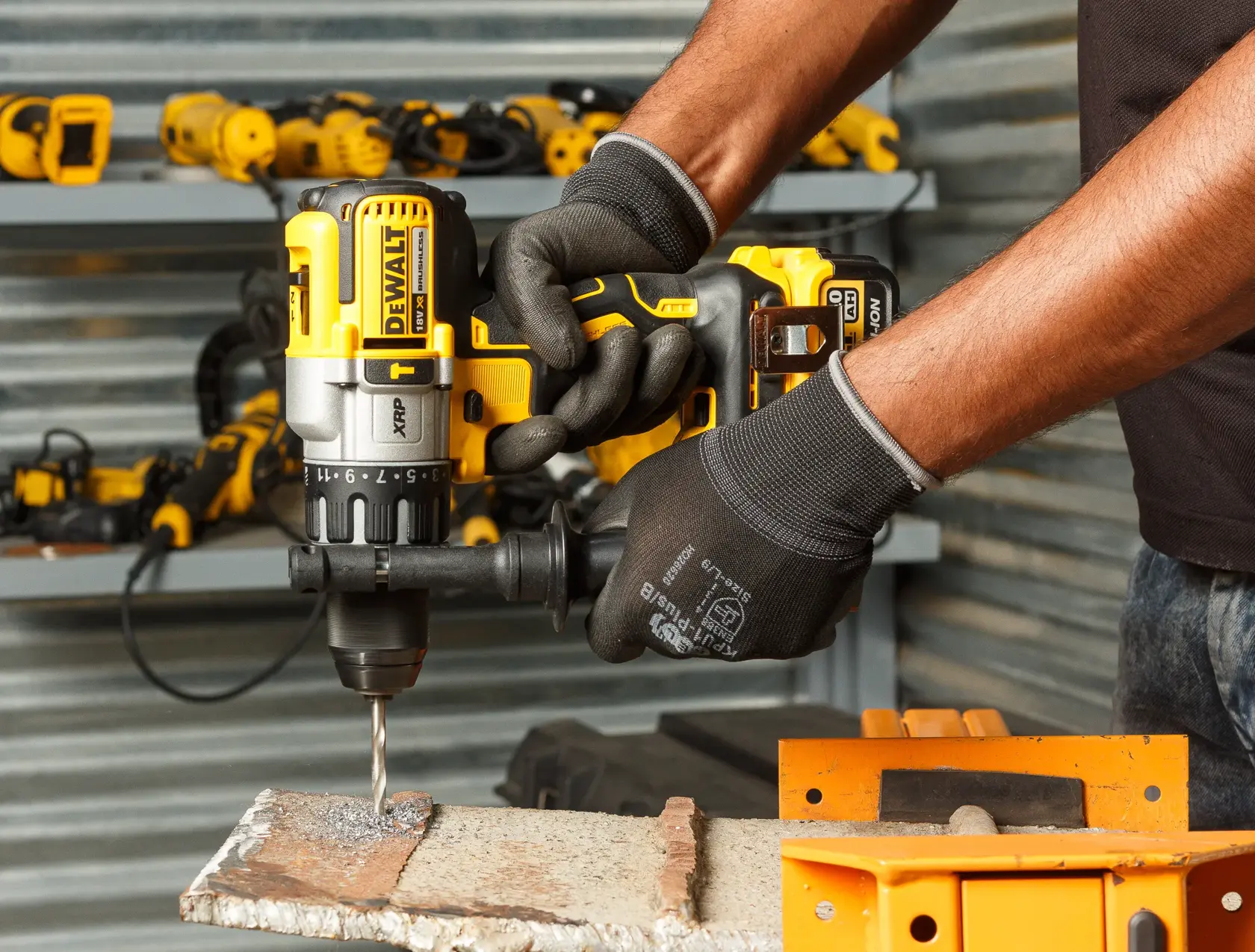 A person uses a DEWALT cordless drill to drill into metal, wearing gloves. Tools are visible on shelves nearby.