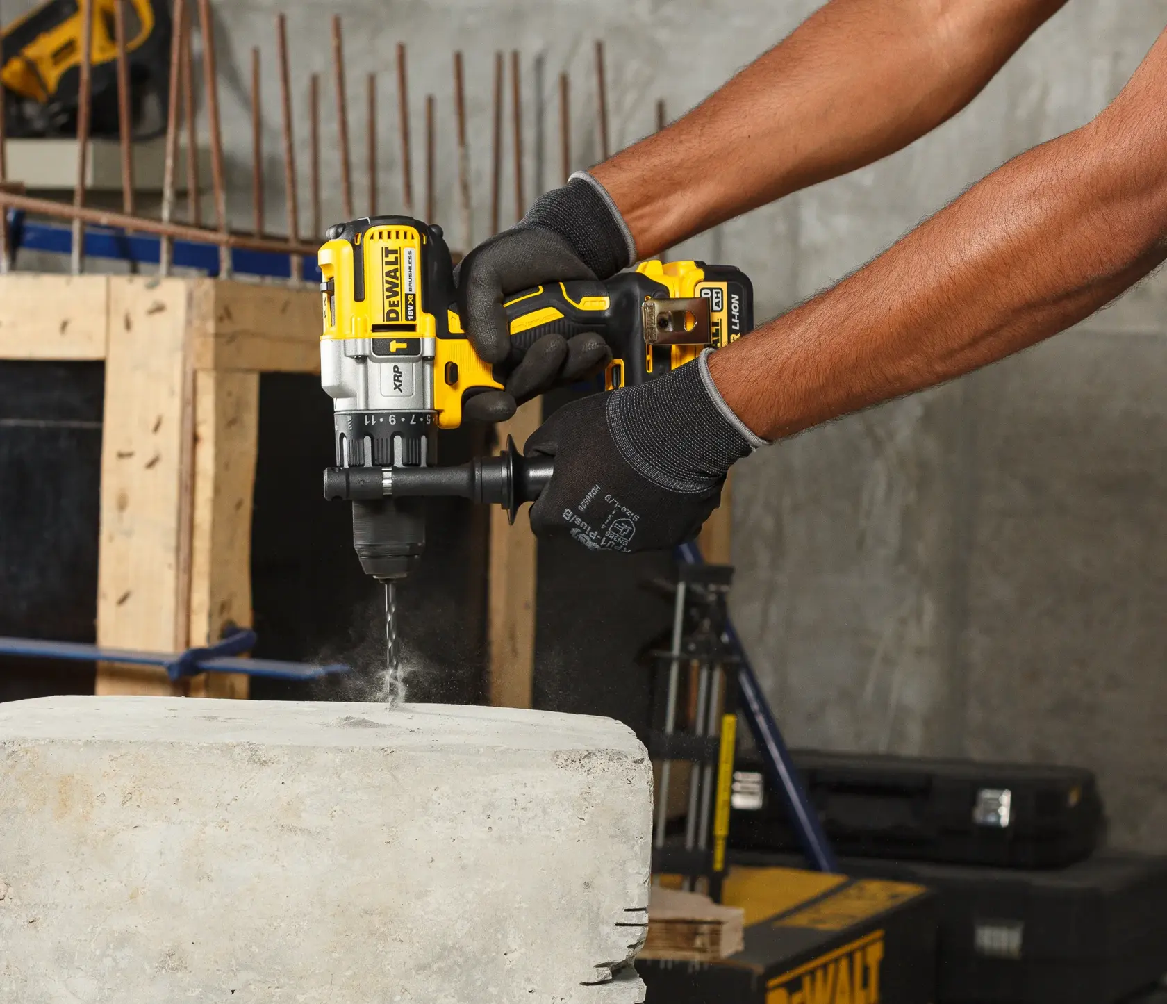 Person uses a DEWALT cordless drill to bore into concrete at a construction site, wearing black gloves.