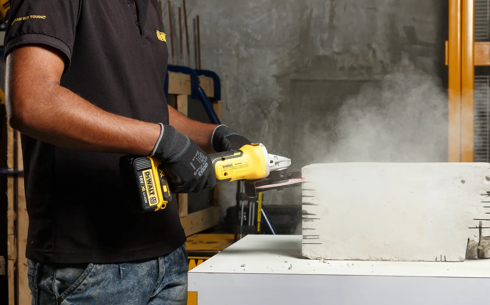 Person using a DEWALT cordless angle grinder on a concrete block, producing dust indoors.