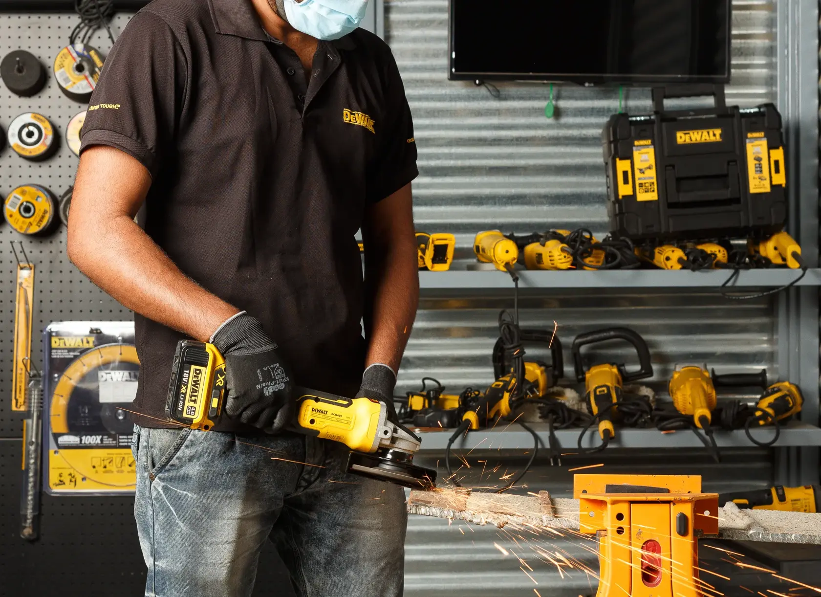 Person uses a DEWALT cordless grinder on metal, wearing gloves and mask. Tools and toolboxes are seen in background.