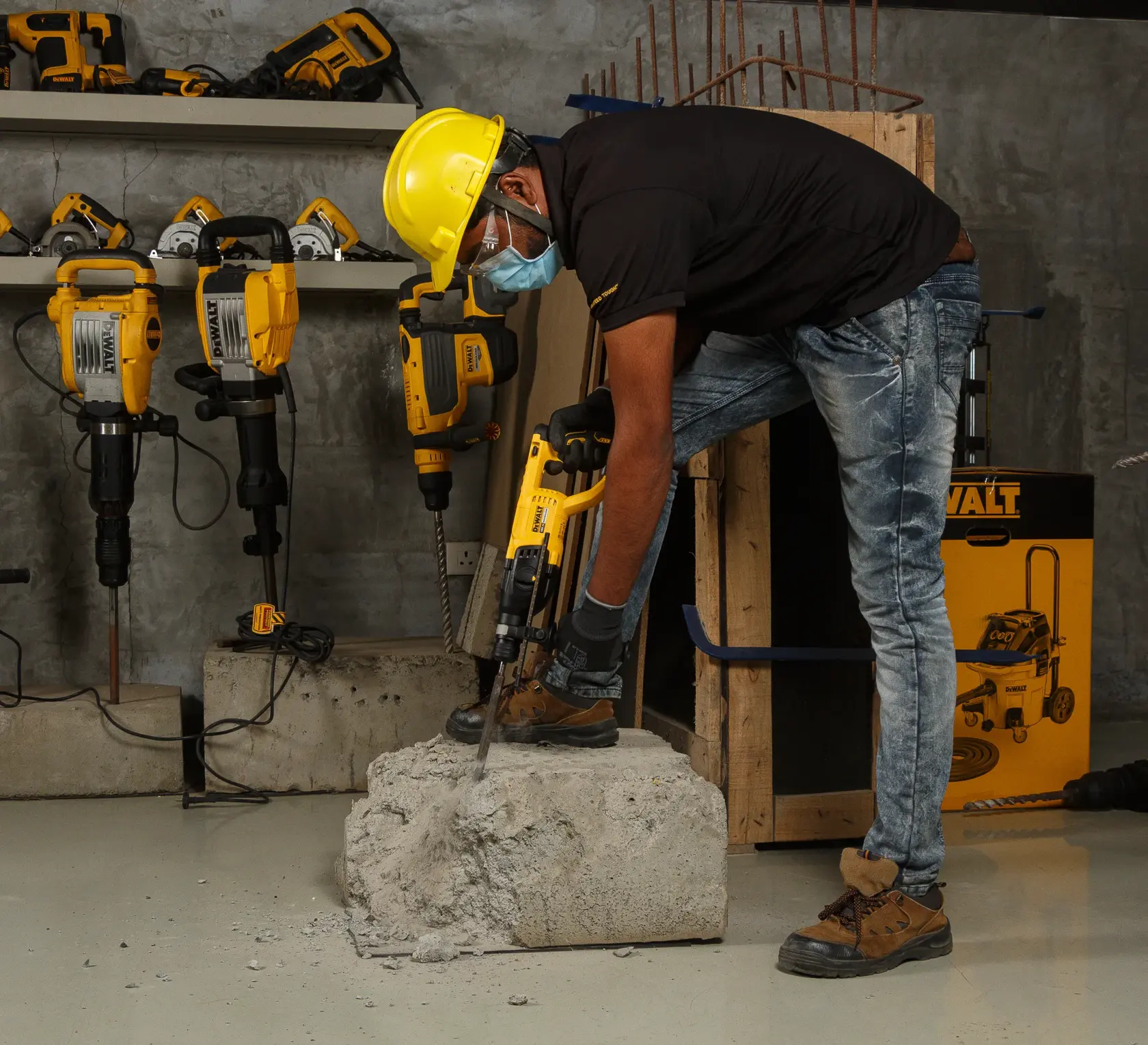 Worker uses a DEWALT hammer drill on concrete, wearing safety gear. Other DEWALT tools are visible on shelves.