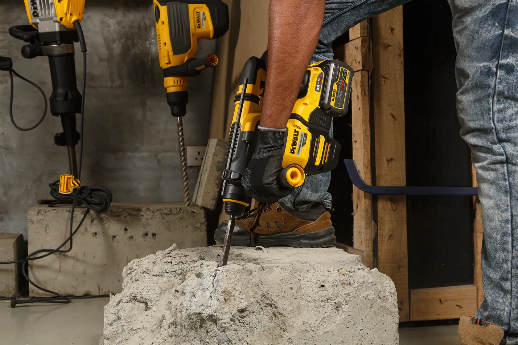 Person using a DEWALT DCH333NT cordless rotary hammer on a concrete block at a construction site.