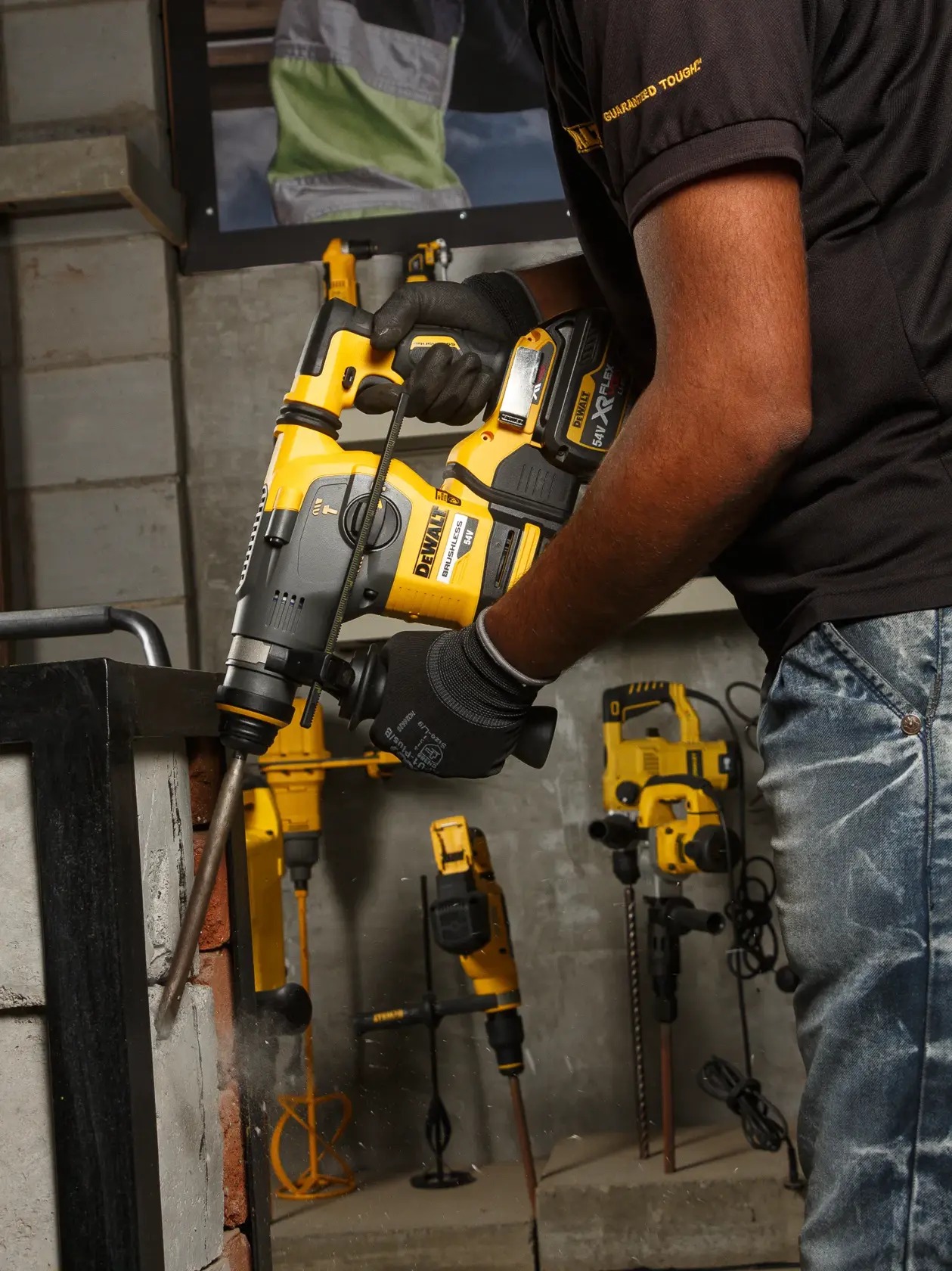Person using DEWALT DCH333NT rotary hammer drill on a brick wall. Other DEWALT tools visible in the background.