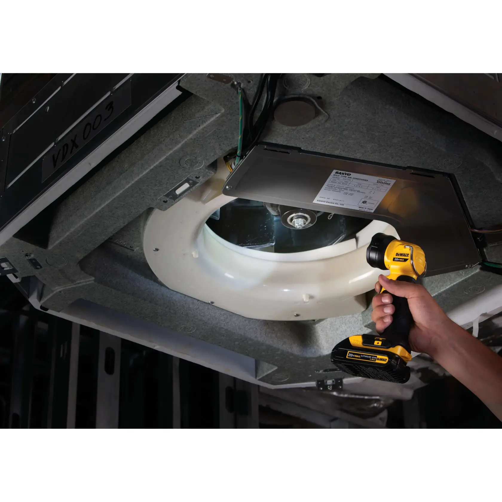 A person uses a DEWALT DCL040 portable LED work light to illuminate the interior components of an air conditioning unit or similar mechanical equipment during maintenance.