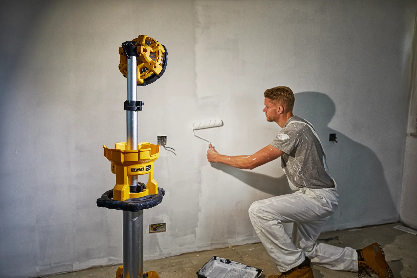 Photo of DEWALT DCL079-XJ, DCL079 work light on tripod illuminating a painter working on a wall indoors.