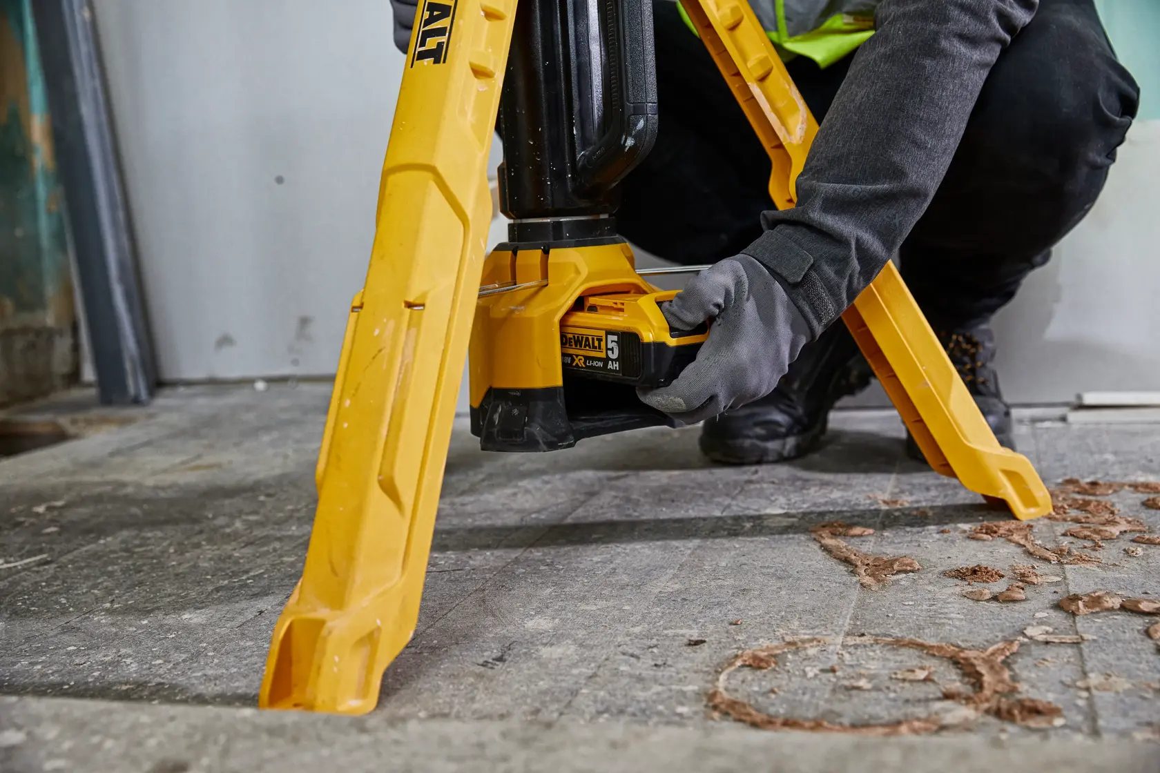 DEWALT site light tripod photographed, SKUs DCL079-XJ, DCL079, worker adjusting battery on construction floor.