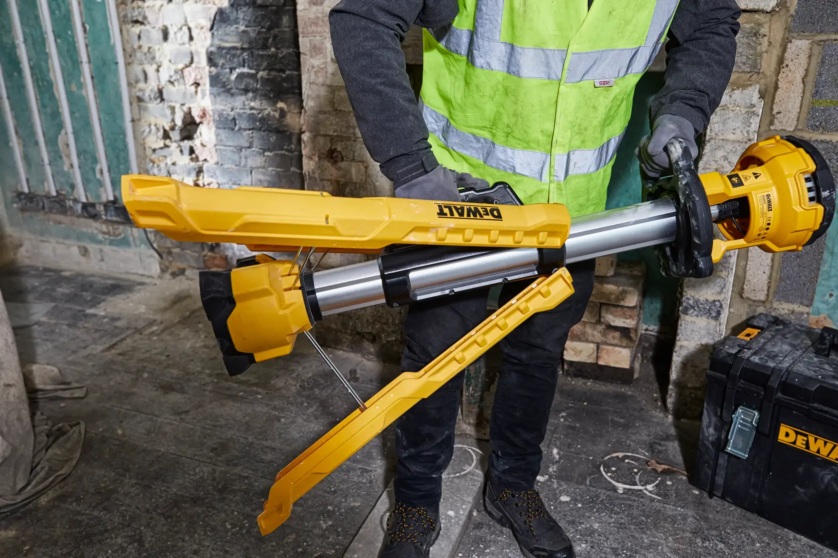DEWALT DCL079-XJ, DCL079 work light with tripod legs, yellow and silver, held by worker in safety vest.
