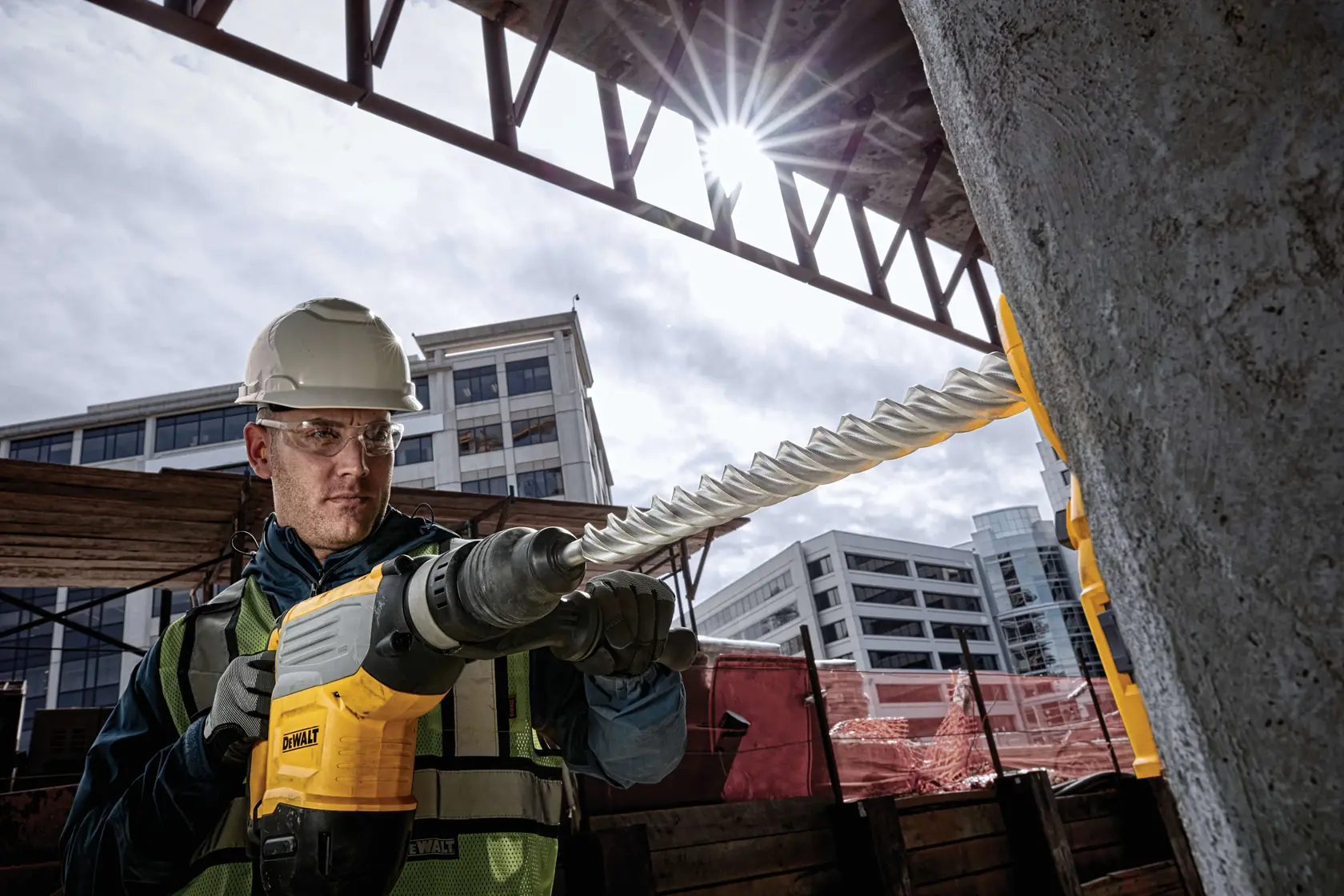 Worker using DEWALT rotary hammer drill with DT60845 bit on concrete at construction site.