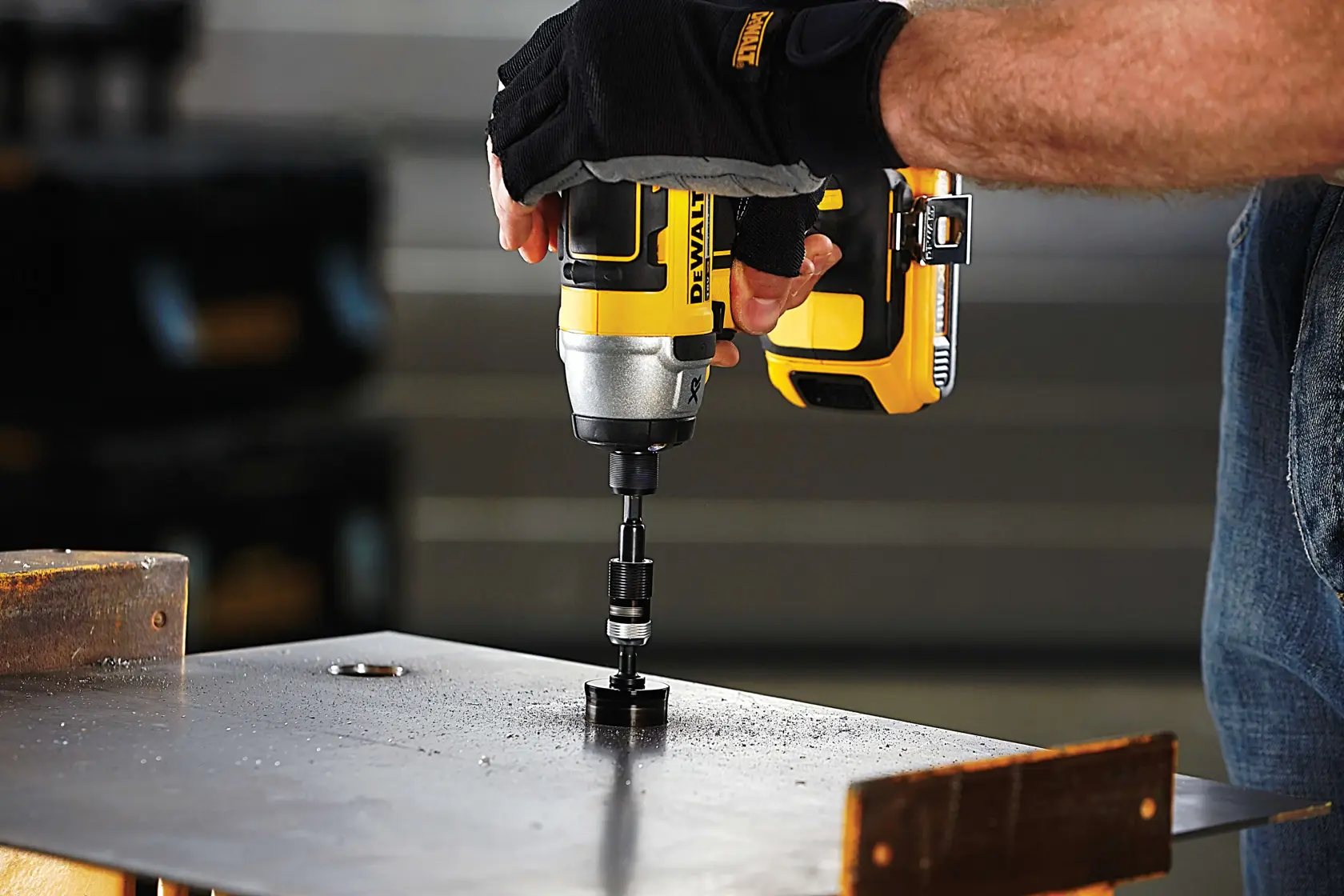 A person uses a DEWALT drill to make a hole in a metal sheet, wearing gloves for protection.