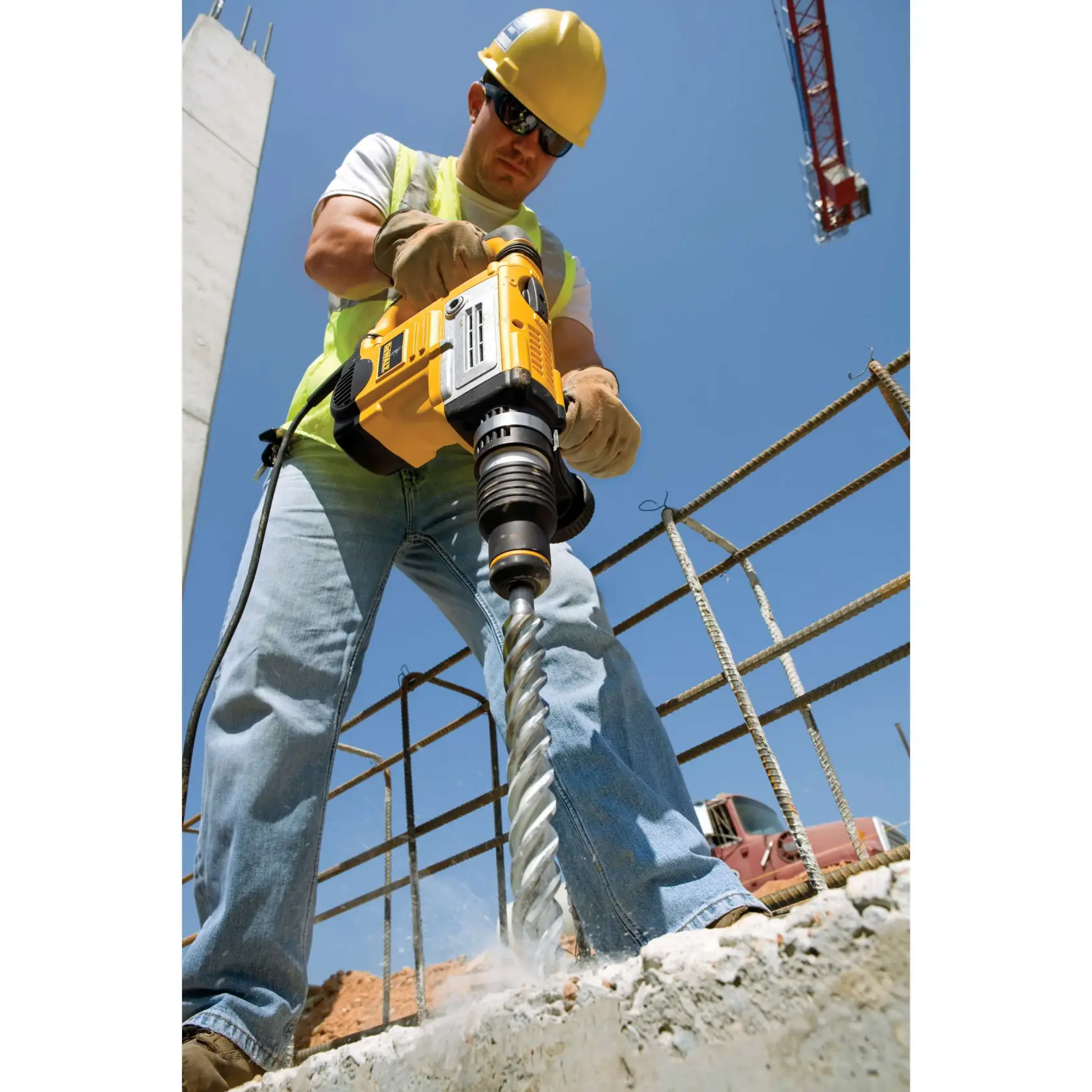 Person using a DEWALT drill on concrete at a construction site on a sunny day.