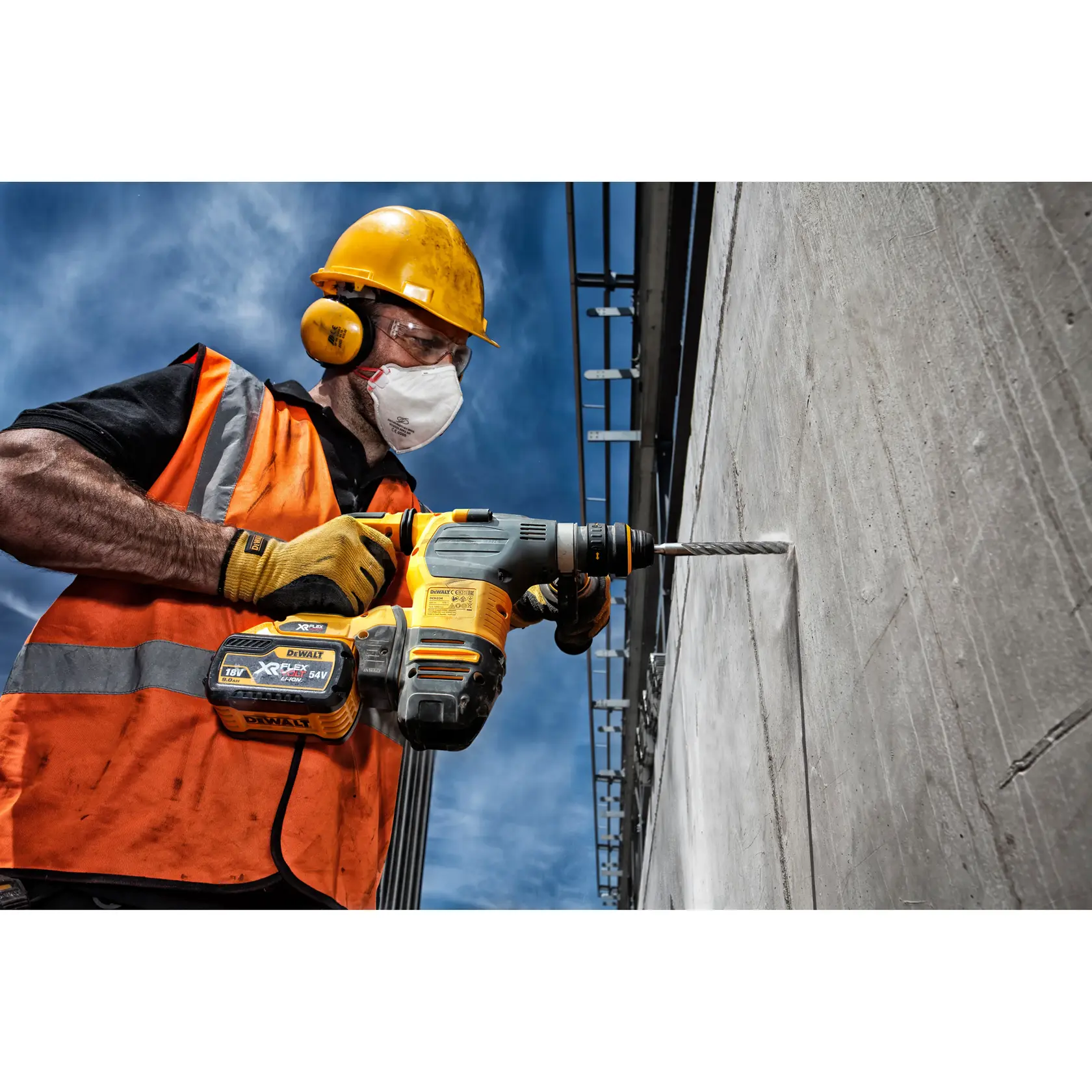 Person using DEWALT drill DT9504 to drill into concrete wall, wearing safety gear and orange vest outdoors.