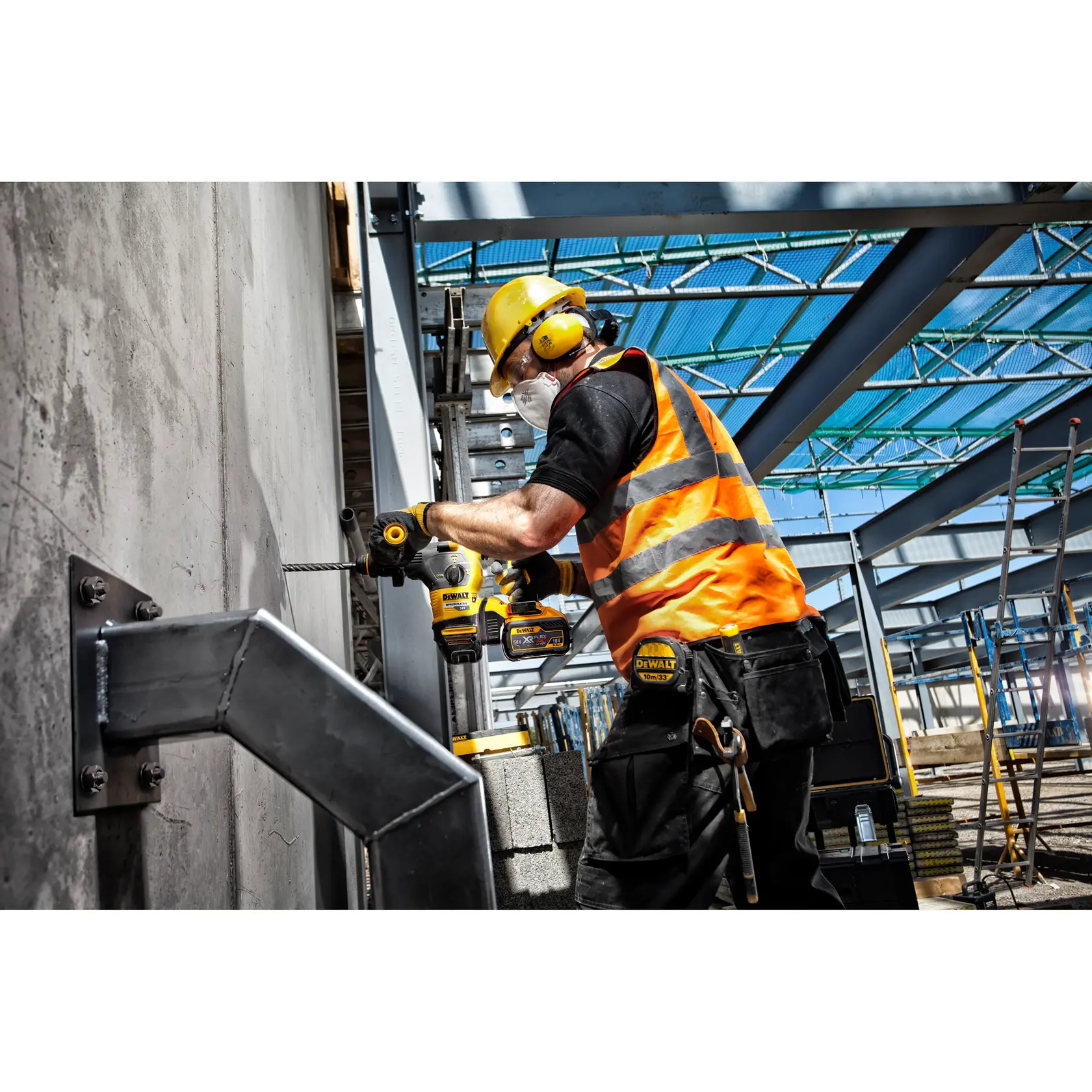 Worker in safety gear drills concrete wall with DEWALT tool at construction site with steel beams.