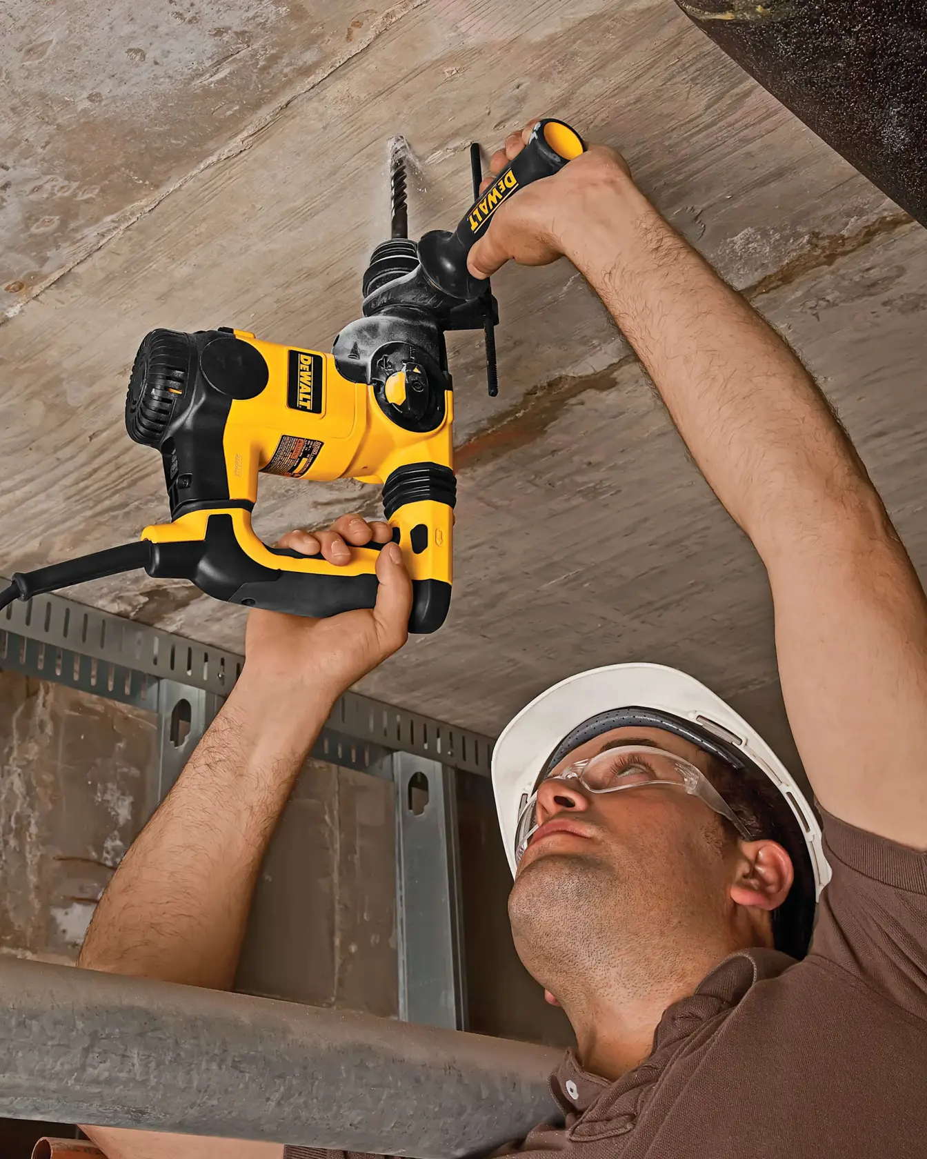 Person using a DEWALT drill to bore into a concrete ceiling while wearing a safety helmet.