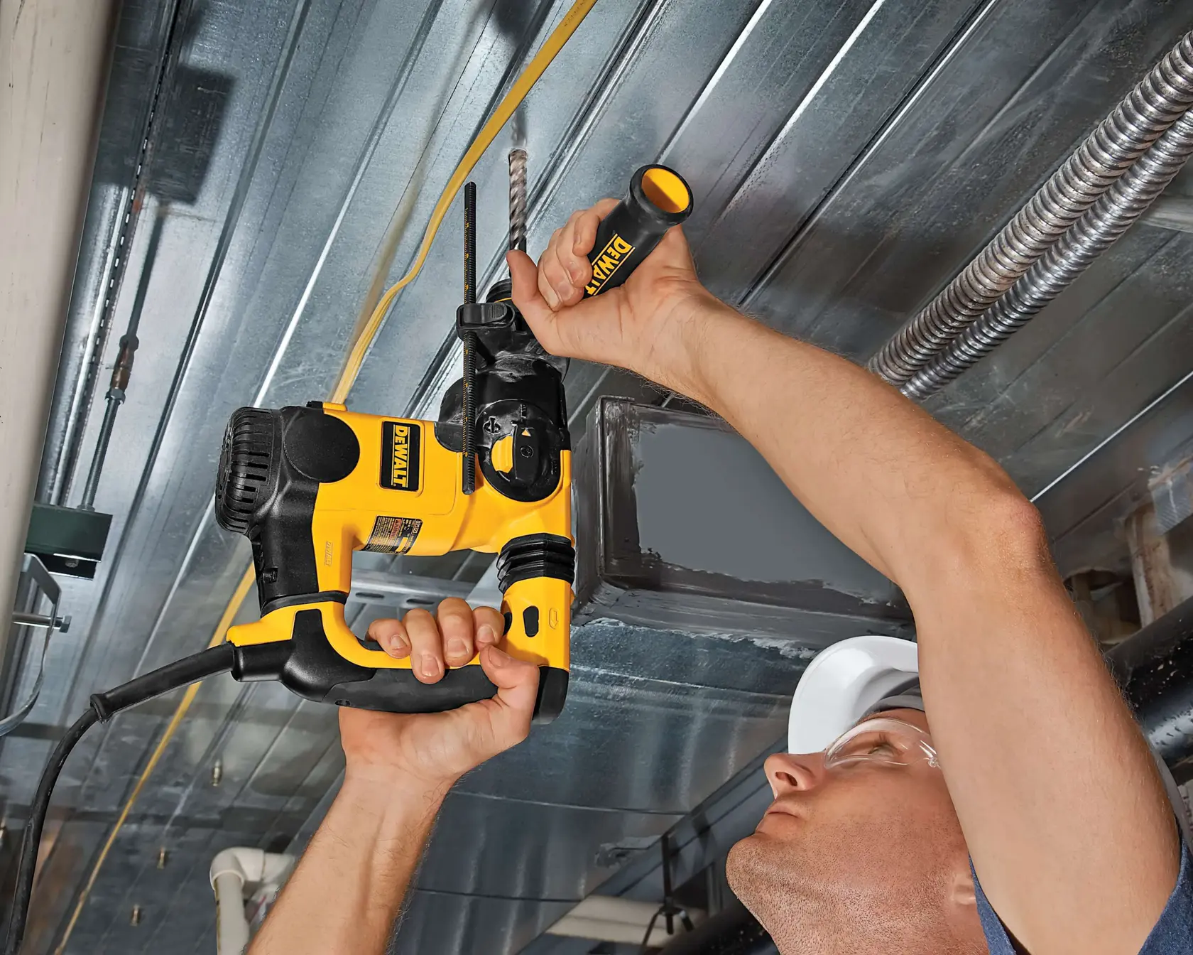 A person uses a DEWALT power drill to work on a metal ceiling, holding the tool and drilling upward.