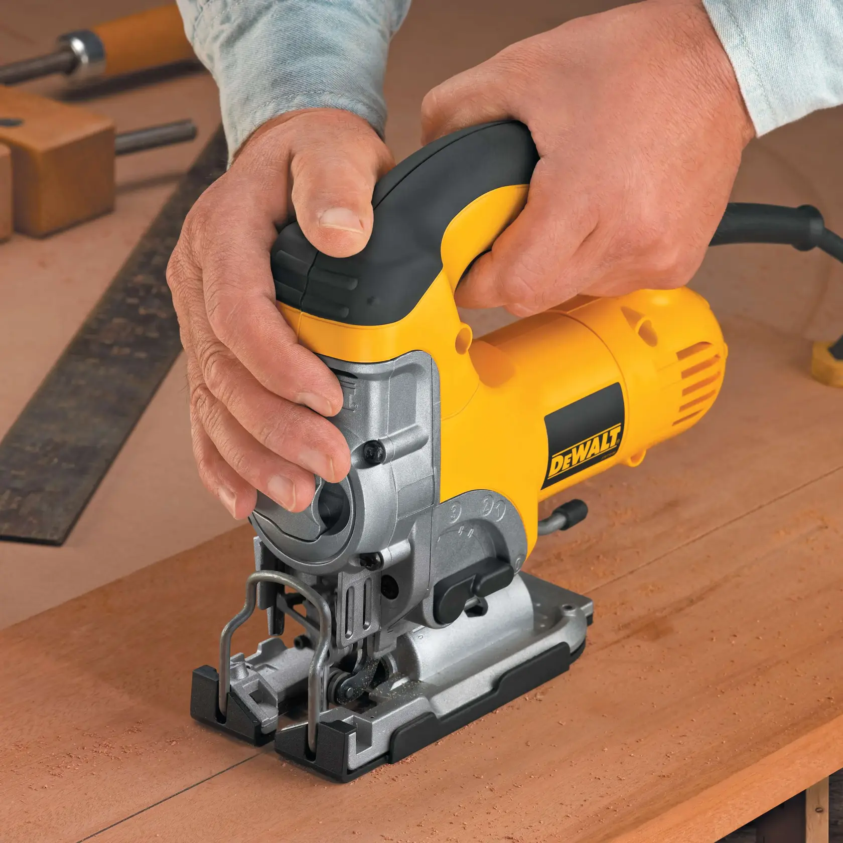 Hands using a DEWALT jigsaw to cut wood on a workbench. Other tools are visible in the background.