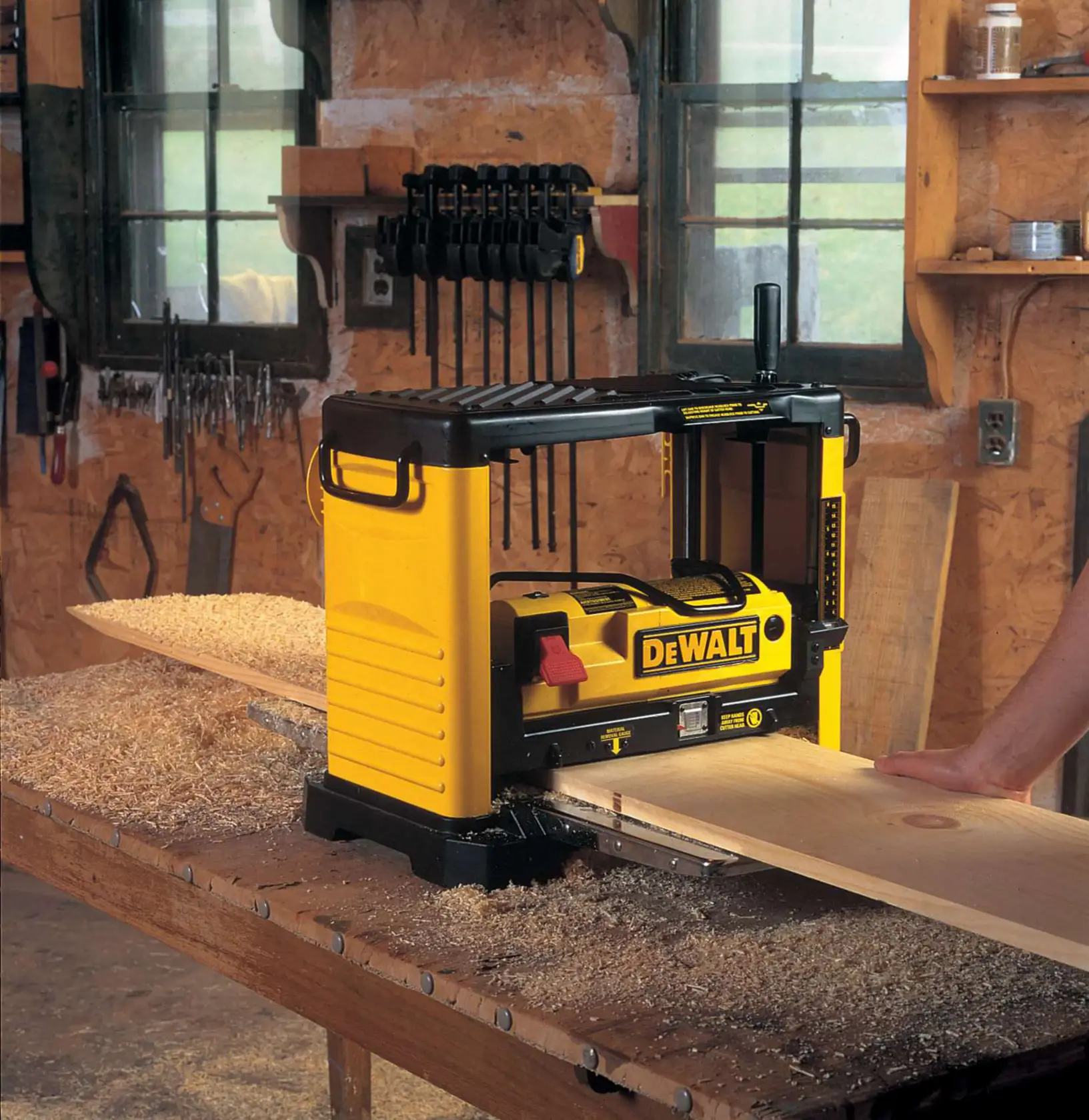DEWALT DW733 planer machine on a workbench in a workshop, processing a wooden board.