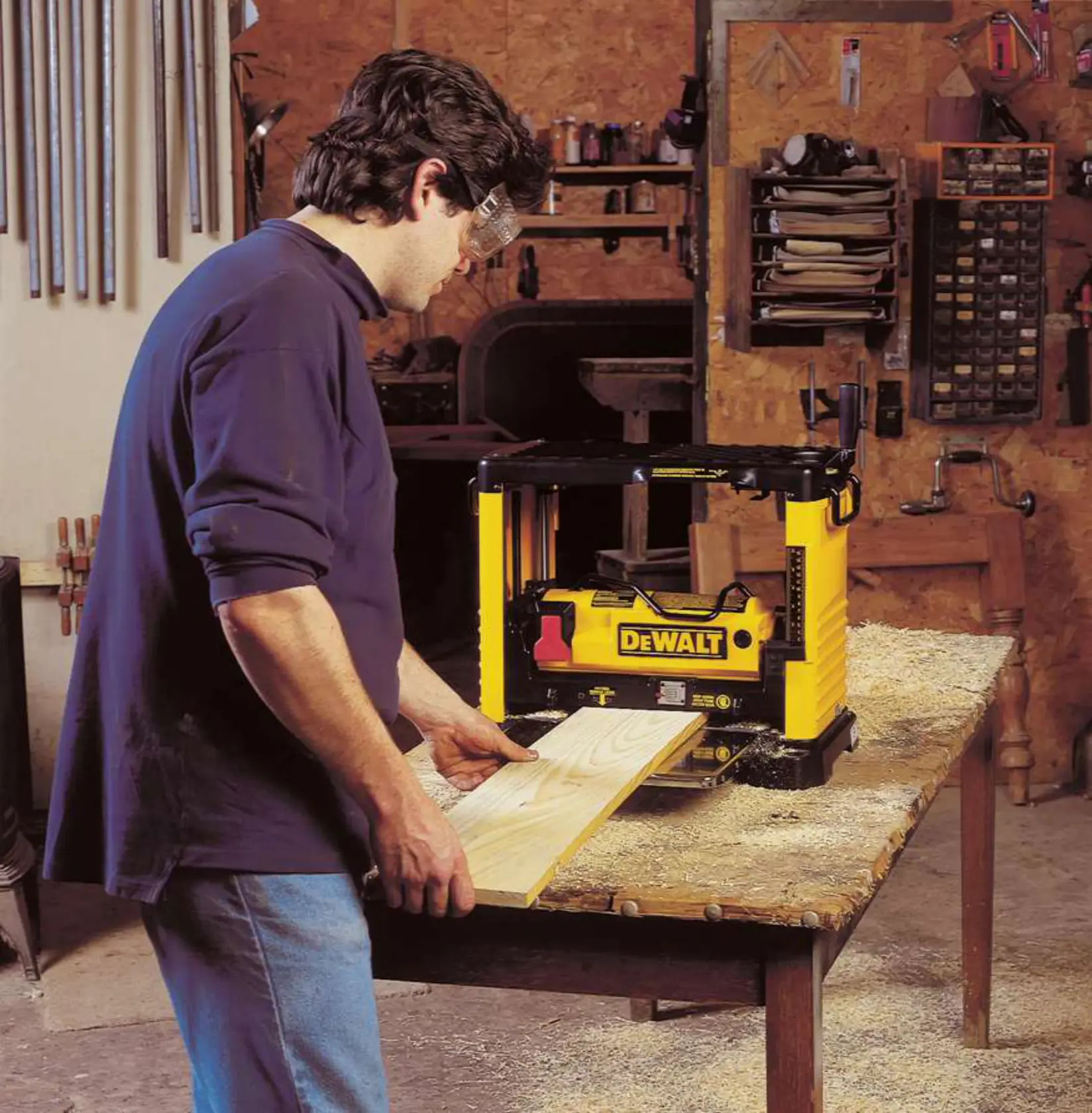Person using a yellow DEWALT DW733 woodworking planer on a workbench in a workshop.