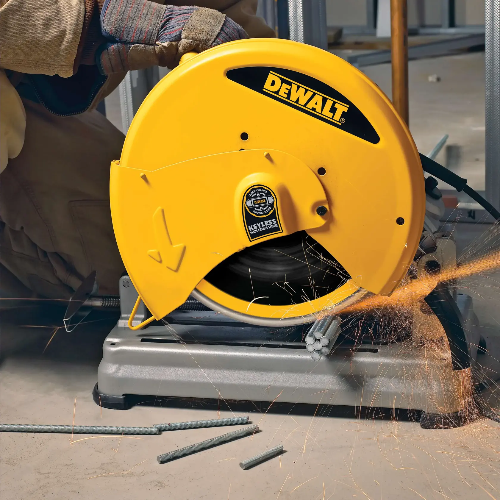 A DEWALT branded chop saw (model DW8500) is being used to cut metal rods. Sparks are visible as the saw blade contacts the material. The operator is wearing protective gloves and operating the tool in an industrial work setting.