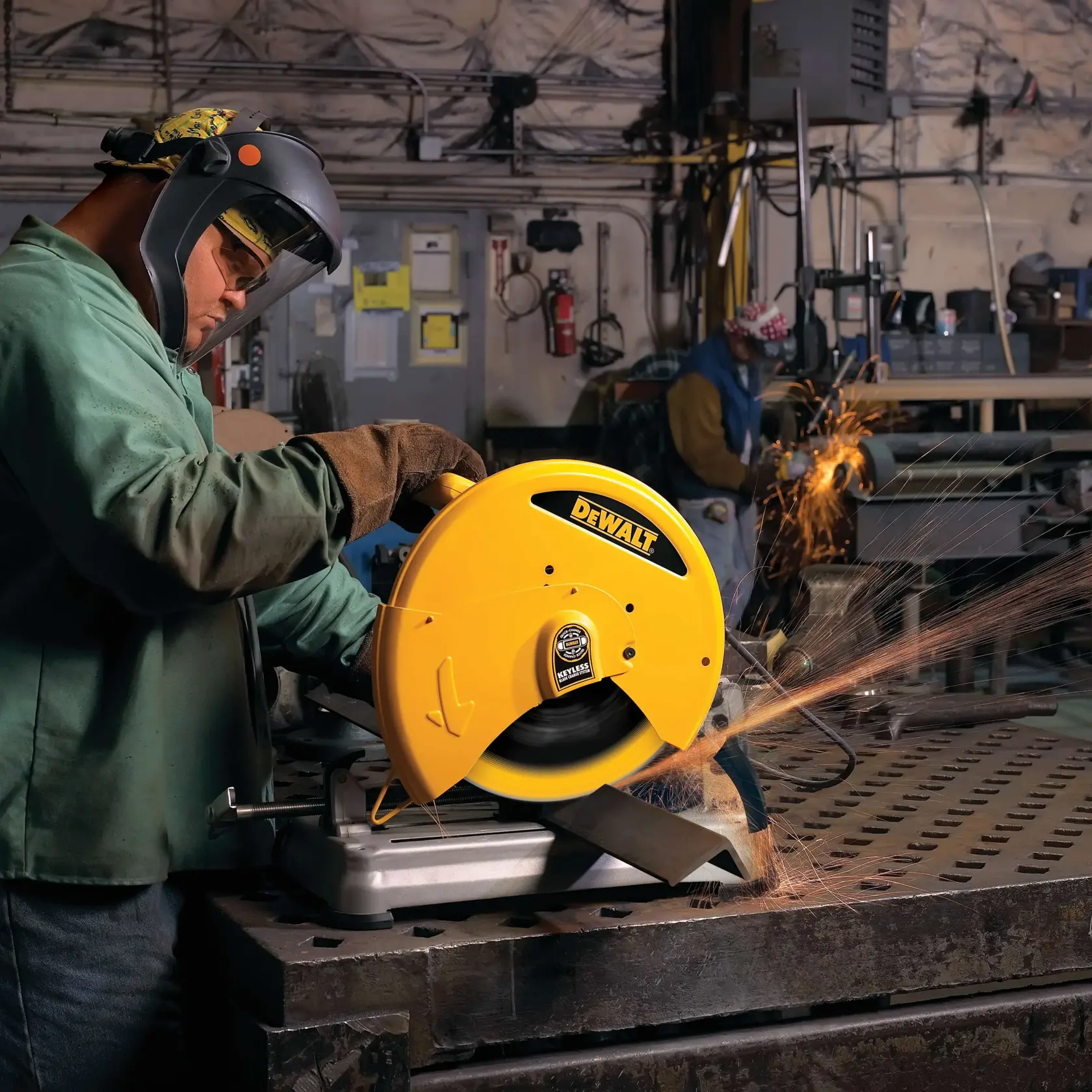 A worker wearing safety gear operates a yellow DEWALT DW8500 cut-off saw in a workshop, cutting metal and producing sparks. Another person in the background is also working with metal.