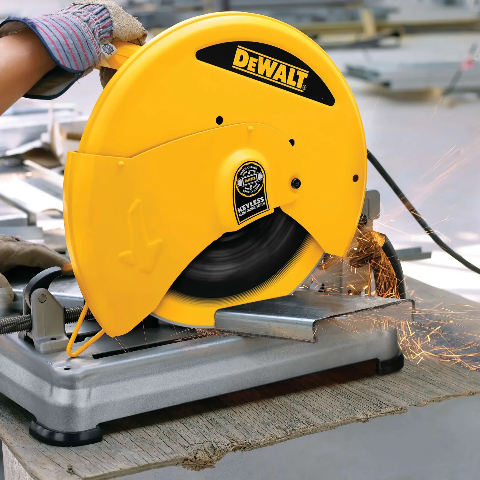 A DEWALT metal cutting saw is being used to cut through a piece of metal. Sparks are flying from the cutting area, and a gloved hand is operating the tool on a workbench.