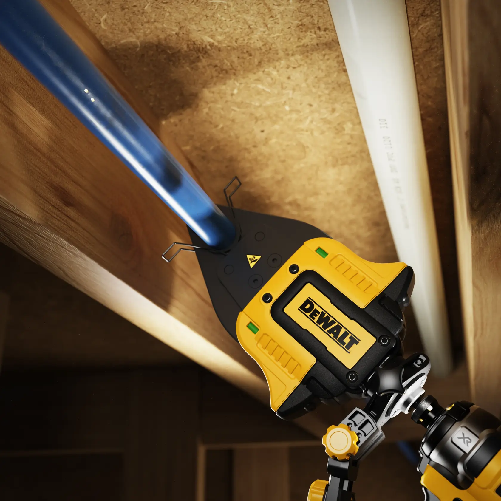 DEWALT tool cuts blue plastic pipe between wooden beams, close view of device in action.