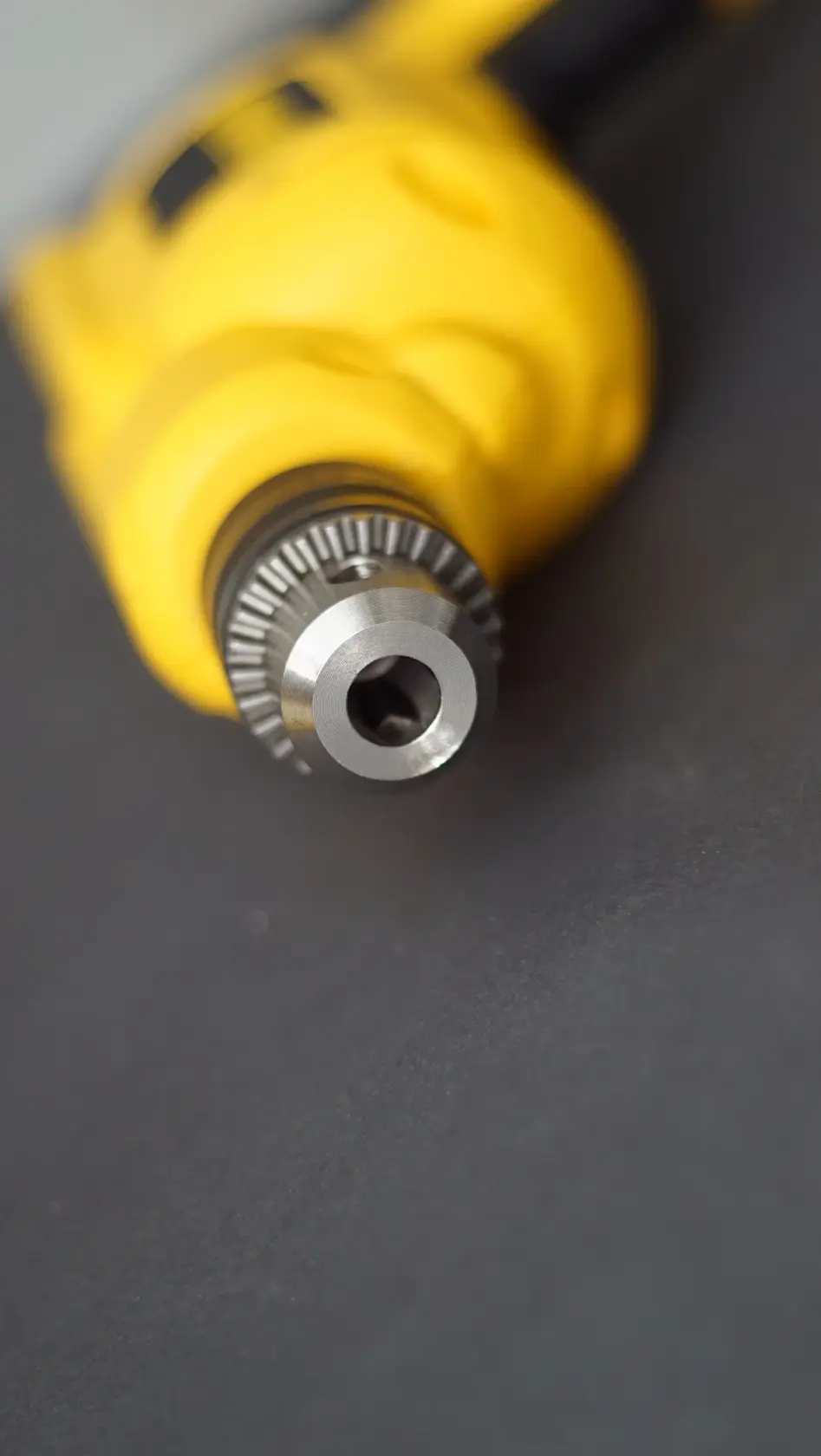 Close-up of the metal chuck of a yellow power drill, with focus on the drill head against a dark surface.