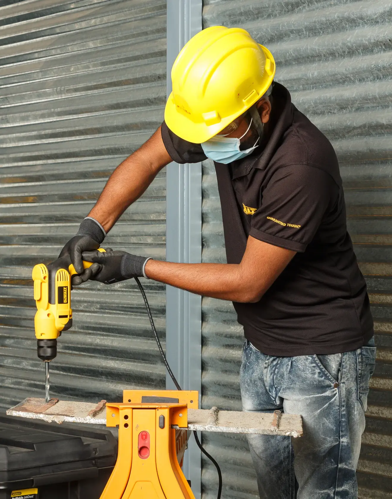 Person using a DEWALT DWD112S corded drill on metal, wearing safety helmet, gloves, and mask.