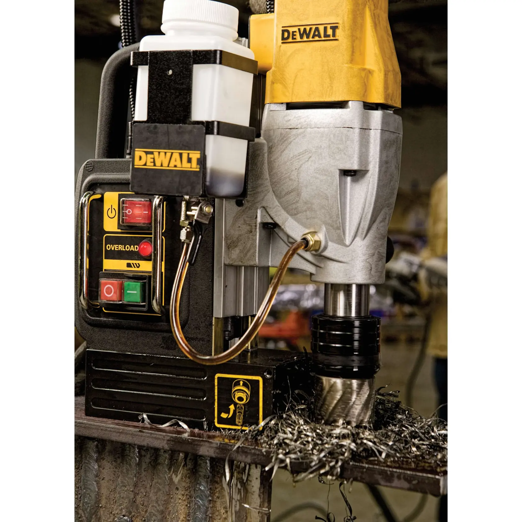 Close-up of a DEWALT magnetic drill press (model DWE1622K) in use, mounted on a metal surface with metal shavings around the drill bit. The control panel with buttons and fluid container are visible.