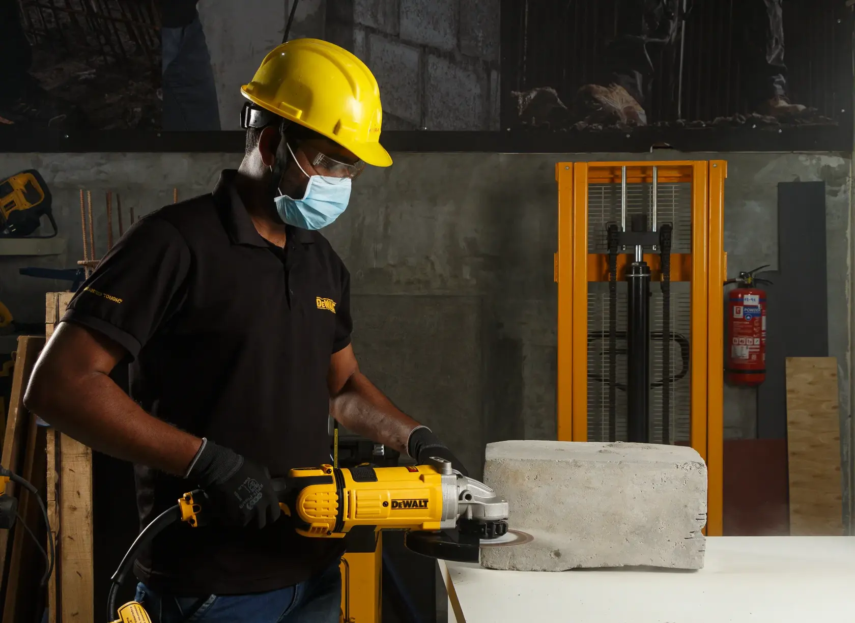Person using a DEWALT grinder to cut concrete block in a workshop, wearing safety gear and gloves.