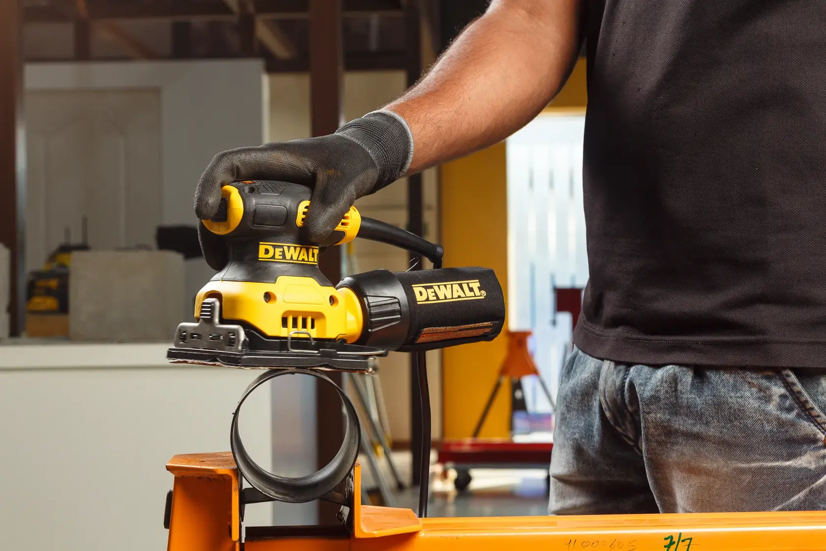 Person using a DEWALT DWE6411 sander on a metal pipe in a workshop setting.