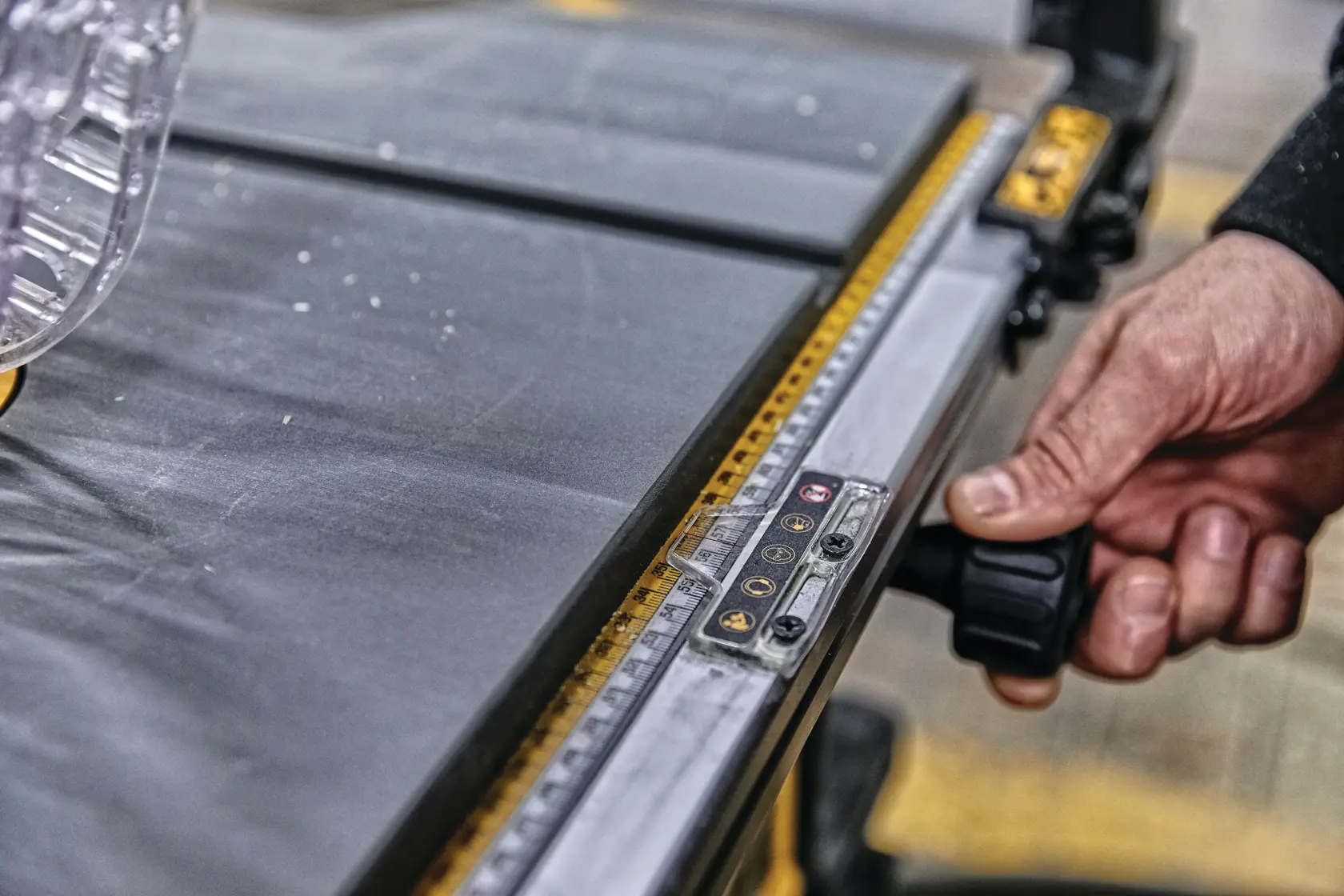 Close-up of a person's hand adjusting the fence of a DEWALT table saw, showing the measuring guide and part of the cutting surface.